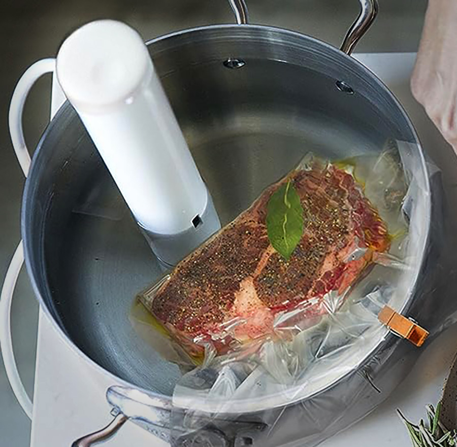 Le Joule Turbo Sous Vide Cooker de Breville est placé dans une casserole avec un steak dans un sachet scellé sous vide.